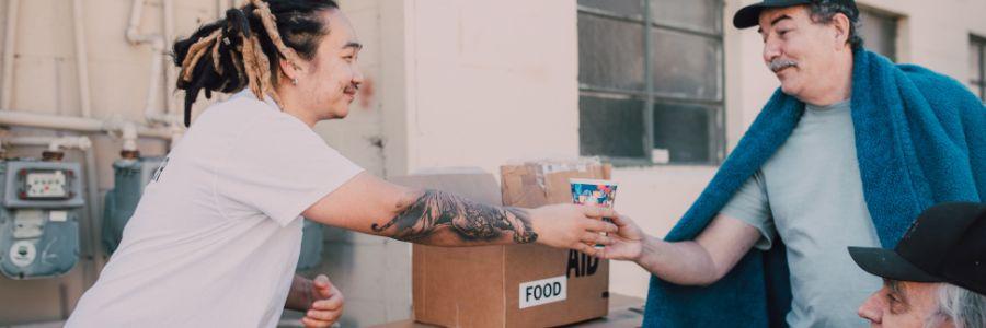 A volunteer hands a cup to a man in need, demonstrating the benefits of giving back to the community through food aid and support. 