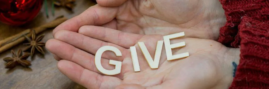Open hands holding wooden letters spelling “GIVE,” symbolizing the Power of Giving through heartfelt, simple acts of kindness.
