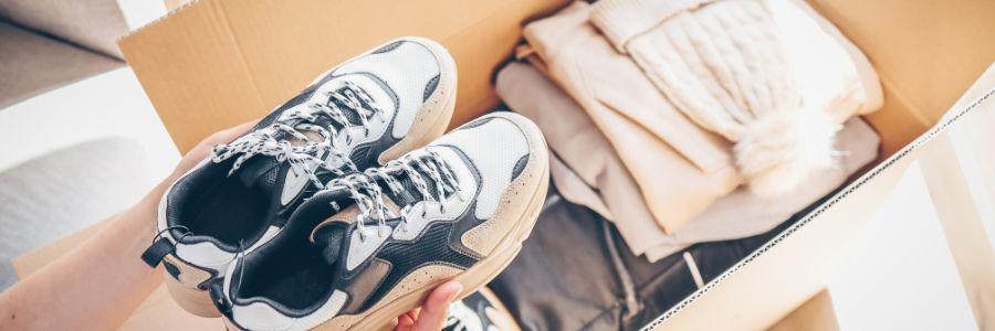Person placing sneakers into a donation box filled with warm clothing, symbolizing the spirit to Give Generously and support those in need.