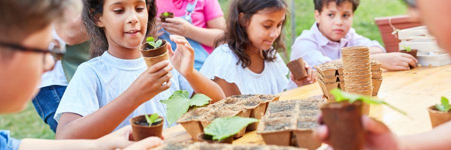 Children planting seedlings in biodegradable pots during an outdoor activity, demonstrating environmental responsibility and joyful giving — a perfect example of day of giving ideas for kids.