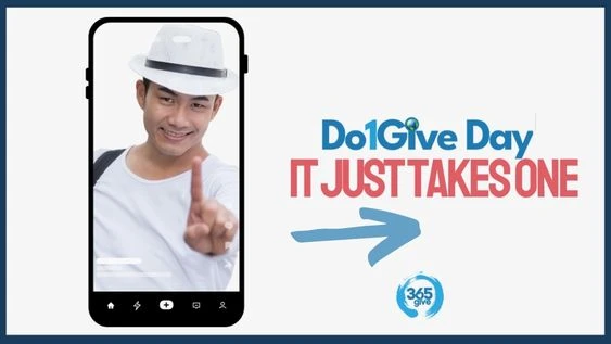 Smiling man holding up one finger on phone screen with Do1Give Day message “It Just Takes One”