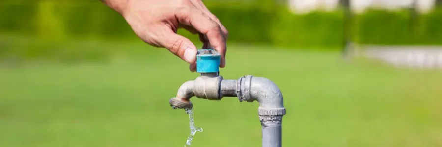 Hand turning off an outdoor water tap to reduce waste and support sustainable water usage practices.