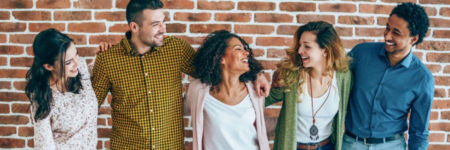 Group of diverse friends smiling and laughing together in front of a brick wall, showing the joy and importance of friendship.