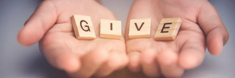 Open hands holding wooden blocks spelling GIVE to symbolize creating a personal giving plan