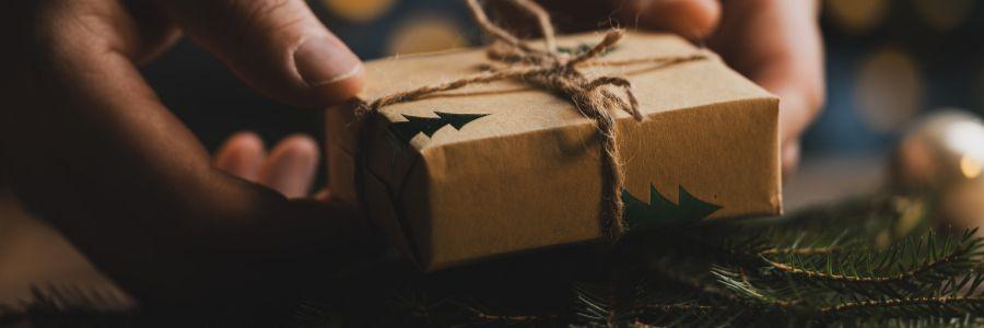 Christmas giving in the holiday season: hands holding a gift wrapped in brown paper and twine