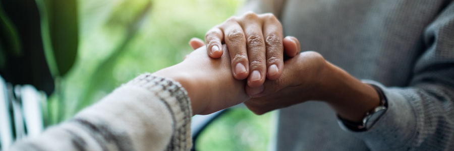 Close-up of one person holding another person’s hands in a supportive, reassuring gesture
