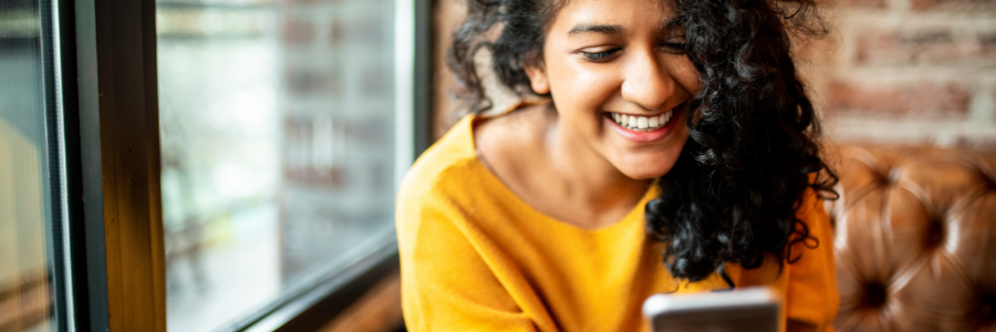 Smiling woman reading a supportive message on her phone, practicing receiving love instead of earning love