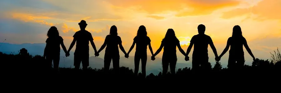 Silhouettes of people holding hands at sunset, symbolizing unity, giving, and shared happiness
