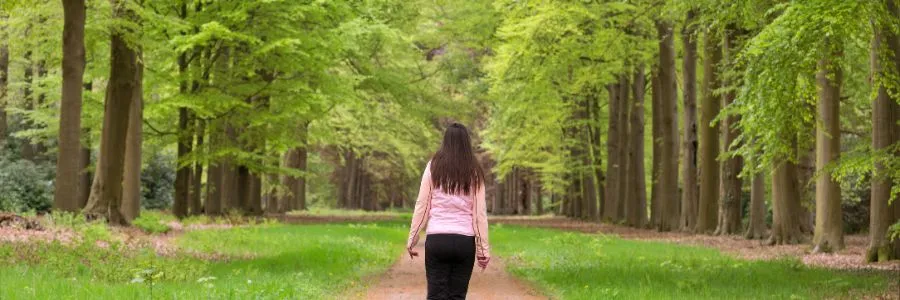 A person walks slowly along a peaceful tree-lined path, practicing Forest Bathing in a calm natural setting.