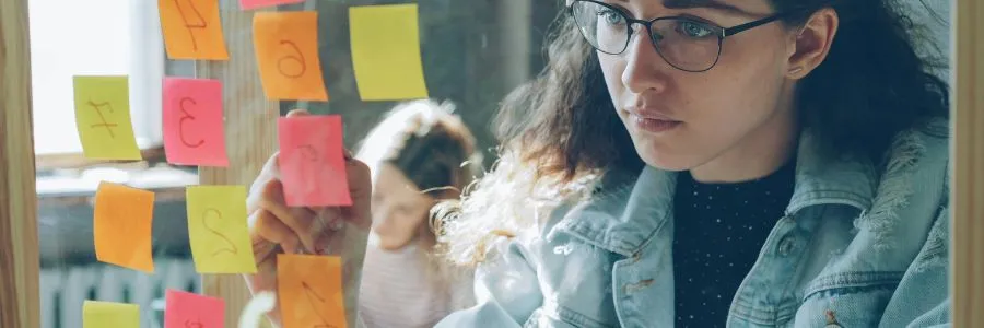  Woman organizing sticky notes on a glass board to plan her day with intention and avoid living on autopilot.
