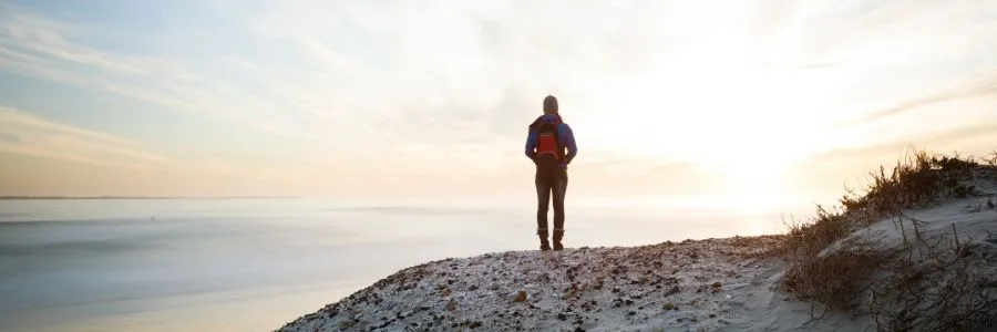 A person standing by the water at sunrise, experiencing a quiet moment of awe in nature.