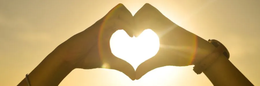 Hands forming a heart shape in sunlight, symbolizing giving, awe, and human connection.