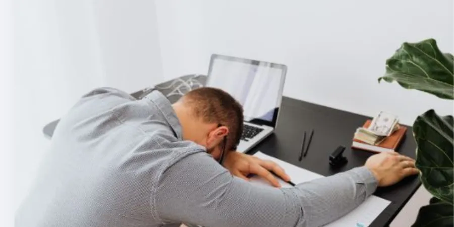 Exhausted man resting his head on his desk while working on a laptop, illustrating workplace stress and burnout.