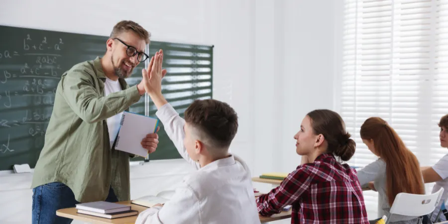 Teacher high-fiving a student in a supportive classroom, building positive teacher student relationships.
