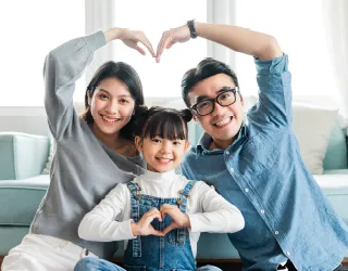 A joyful family sitting together, forming heart shapes with their hands, symbolizing love and unity.