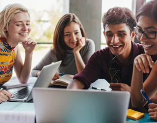 A group of young leaders engaged in a discussion around a laptop, planning a collaborative activity for a youth leadership club.