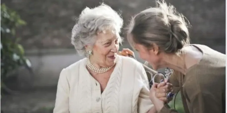 A younger woman shares a warm moment with an elderly woman, smiling and holding her hand, highlighting how helping others builds happiness and meaningful connections.