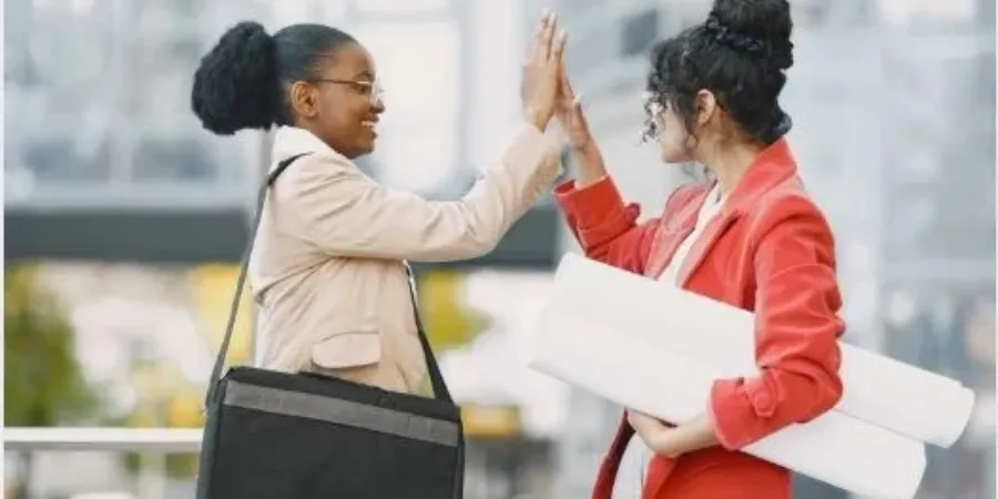 Two female colleagues exchange a high-five outdoors, celebrating teamwork, mutual support, and the happiness that comes from helping others.