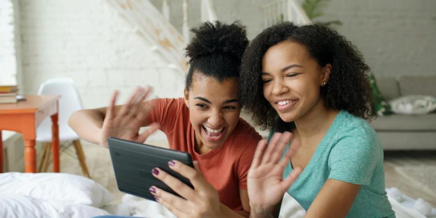 Two women smiling and waving during a video call on a tablet.